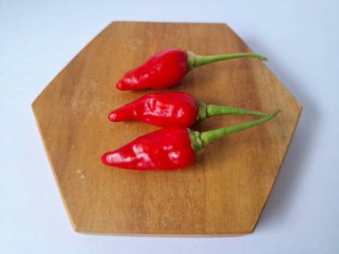 Ahşap servis tahtasında kırmızı kırmızıbiber. Kırmızı biber, acı bir tadı olan ve genellikle yemek ve tıpta kullanılan bir kırmızı biber türüdür. Bu biber ince şekli, parlak kırmızı rengi ve yüksek baharat seviyesi ile bilinir.