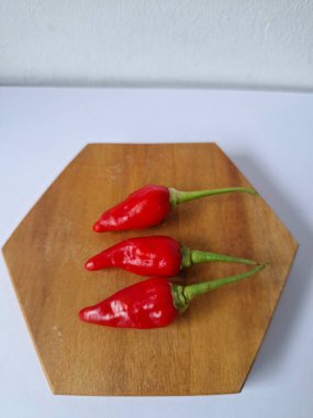 Ahşap servis tahtasında kırmızı kırmızıbiber. Kırmızı biber, acı bir tadı olan ve genellikle yemek ve tıpta kullanılan bir kırmızı biber türüdür. Bu biber ince şekli, parlak kırmızı rengi ve yüksek baharat seviyesi ile bilinir.