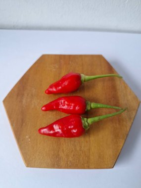 Ahşap servis tahtasında kırmızı kırmızıbiber. Kırmızı biber, acı bir tadı olan ve genellikle yemek ve tıpta kullanılan bir kırmızı biber türüdür. Bu biber ince şekli, parlak kırmızı rengi ve yüksek baharat seviyesi ile bilinir.