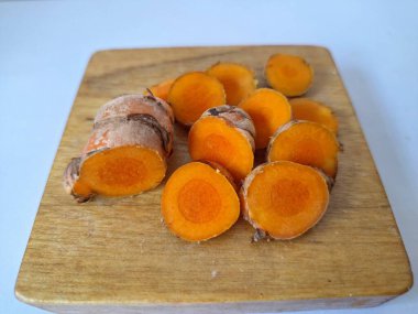 Servis tahtasında taze zerdeçal yumrusu dilimleri. Bu baharat Asya mutfağında yaygın olarak kullanılır, özellikle köri gibi yemeklerde tat ve renk için. Zerdeçal ayrıca aktif bileşik curkiminle birlikte tıbbi özelliklere de sahiptir.