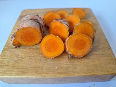 Servis tahtasında taze zerdeçal yumrusu dilimleri. Bu baharat Asya mutfağında yaygın olarak kullanılır, özellikle köri gibi yemeklerde tat ve renk için. Zerdeçal ayrıca aktif bileşik curkiminle birlikte tıbbi özelliklere de sahiptir.