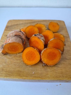 Servis tahtasında taze zerdeçal yumrusu dilimleri. Bu baharat Asya mutfağında yaygın olarak kullanılır, özellikle köri gibi yemeklerde tat ve renk için. Zerdeçal ayrıca aktif bileşik curkiminle birlikte tıbbi özelliklere de sahiptir.