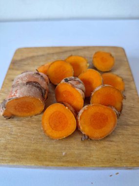 Servis tahtasında taze zerdeçal yumrusu dilimleri. Bu baharat Asya mutfağında yaygın olarak kullanılır, özellikle köri gibi yemeklerde tat ve renk için. Zerdeçal ayrıca aktif bileşik curkiminle birlikte tıbbi özelliklere de sahiptir.