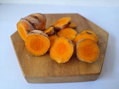 Servis tahtasında taze zerdeçal yumrusu dilimleri. Bu baharat Asya mutfağında yaygın olarak kullanılır, özellikle köri gibi yemeklerde tat ve renk için. Zerdeçal ayrıca aktif bileşik curkiminle birlikte tıbbi özelliklere de sahiptir.