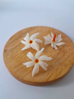 Yuvarlak tahta üzerinde taze parijat çiçekleri. Çeşitli kullanımları var, hem tıbbi hem de kültürel. Ayurvedic tıpta ateş, öksürük ve soğuk algınlığını tedavi etmek için kullanılır. Çiçekler Hindu ayinlerinde ve tanrılara adak olarak da kullanılır.