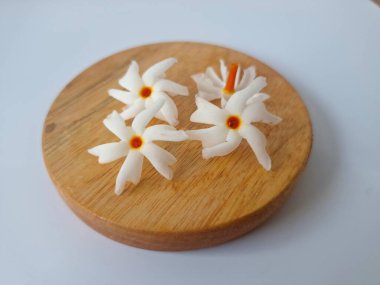 Yuvarlak tahta üzerinde taze parijat çiçekleri. Çeşitli kullanımları var, hem tıbbi hem de kültürel. Ayurvedic tıpta ateş, öksürük ve soğuk algınlığını tedavi etmek için kullanılır. Çiçekler Hindu ayinlerinde ve tanrılara adak olarak da kullanılır.