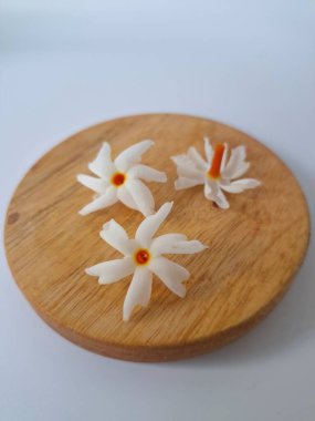 Yuvarlak tahta üzerinde taze parijat çiçekleri. Çeşitli kullanımları var, hem tıbbi hem de kültürel. Ayurvedic tıpta ateş, öksürük ve soğuk algınlığını tedavi etmek için kullanılır. Çiçekler Hindu ayinlerinde ve tanrılara adak olarak da kullanılır.