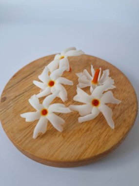 Yuvarlak tahta üzerinde taze parijat çiçekleri. Çeşitli kullanımları var, hem tıbbi hem de kültürel. Ayurvedic tıpta ateş, öksürük ve soğuk algınlığını tedavi etmek için kullanılır. Çiçekler Hindu ayinlerinde ve tanrılara adak olarak da kullanılır.