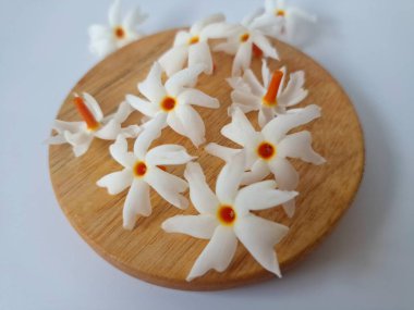 Yuvarlak tahta üzerinde taze parijat çiçekleri. Çeşitli kullanımları var, hem tıbbi hem de kültürel. Ayurvedic tıpta ateş, öksürük ve soğuk algınlığını tedavi etmek için kullanılır. Çiçekler Hindu ayinlerinde ve tanrılara adak olarak da kullanılır.