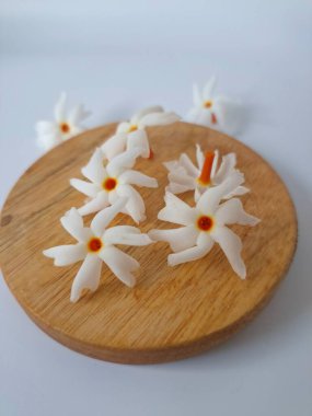 Yuvarlak tahta üzerinde taze parijat çiçekleri. Çeşitli kullanımları var, hem tıbbi hem de kültürel. Ayurvedic tıpta ateş, öksürük ve soğuk algınlığını tedavi etmek için kullanılır. Çiçekler Hindu ayinlerinde ve tanrılara adak olarak da kullanılır.