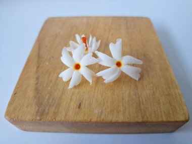 Servis tahtasındaki taze parijat çiçekleri. Çeşitli kullanımları var, hem tıbbi hem de kültürel. Ayurvedic tıpta ateş, öksürük ve soğuk algınlığını tedavi etmek için kullanılır. Çiçekler Hindu ayinlerinde ve tanrılara adak olarak da kullanılır.