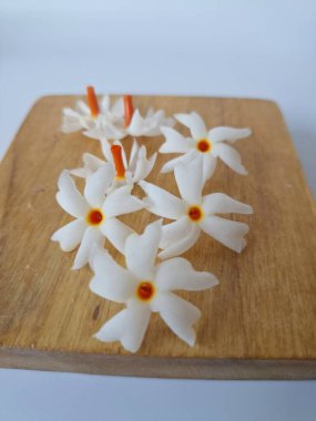 Servis tahtasındaki taze parijat çiçekleri. Çeşitli kullanımları var, hem tıbbi hem de kültürel. Ayurvedic tıpta ateş, öksürük ve soğuk algınlığını tedavi etmek için kullanılır. Çiçekler Hindu ayinlerinde ve tanrılara adak olarak da kullanılır.