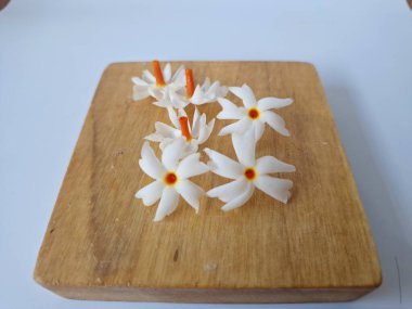 Servis tahtasındaki taze parijat çiçekleri. Çeşitli kullanımları var, hem tıbbi hem de kültürel. Ayurvedic tıpta ateş, öksürük ve soğuk algınlığını tedavi etmek için kullanılır. Çiçekler Hindu ayinlerinde ve tanrılara adak olarak da kullanılır.