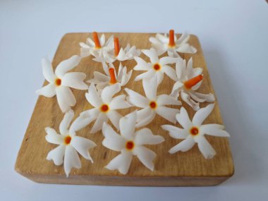 Servis tahtasındaki taze parijat çiçekleri. Çeşitli kullanımları var, hem tıbbi hem de kültürel. Ayurvedic tıpta ateş, öksürük ve soğuk algınlığını tedavi etmek için kullanılır. Çiçekler Hindu ayinlerinde ve tanrılara adak olarak da kullanılır.