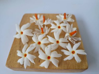 Servis tahtasındaki taze parijat çiçekleri. Çeşitli kullanımları var, hem tıbbi hem de kültürel. Ayurvedic tıpta ateş, öksürük ve soğuk algınlığını tedavi etmek için kullanılır. Çiçekler Hindu ayinlerinde ve tanrılara adak olarak da kullanılır.