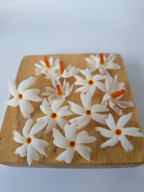 Servis tahtasındaki taze parijat çiçekleri. Çeşitli kullanımları var, hem tıbbi hem de kültürel. Ayurvedic tıpta ateş, öksürük ve soğuk algınlığını tedavi etmek için kullanılır. Çiçekler Hindu ayinlerinde ve tanrılara adak olarak da kullanılır.