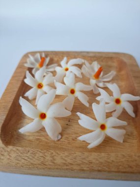 Servis tahtasındaki taze parijat çiçekleri. Çeşitli kullanımları var, hem tıbbi hem de kültürel. Ayurvedic tıpta ateş, öksürük ve soğuk algınlığını tedavi etmek için kullanılır. Çiçekler Hindu ayinlerinde ve tanrılara adak olarak da kullanılır.