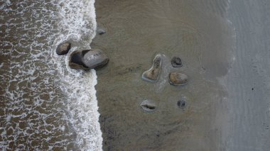 Kumlu deniz tabanına saçılmış pürüzsüz granit taşlardan oluşan hava manzarası gelgit dalgalarıyla yavaşça kıvrılarak kaya ve deniz arasındaki ebedi dansı gözler önüne seriyor..