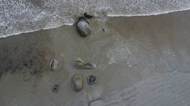 Kumlu deniz tabanına saçılmış pürüzsüz granit taşlardan oluşan hava manzarası gelgit dalgalarıyla yavaşça kıvrılarak kaya ve deniz arasındaki ebedi dansı gözler önüne seriyor..