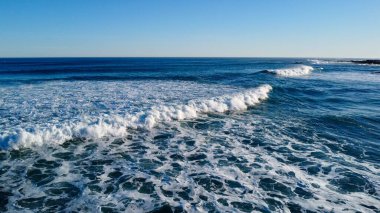 Yumuşak sabah ışığı, dağılmış ayak izleriyle işaretlenmiş el değmemiş kumları aydınlatır. Dalgaların sonsuz kobalt gökyüzünün altında kıyıda tur attığı yerde yalnızlık ve deniz tarafından sessiz bir yansıma hissi uyandırır..