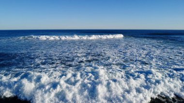 Yumuşak sabah ışığı, dağılmış ayak izleriyle işaretlenmiş el değmemiş kumları aydınlatır. Dalgaların sonsuz kobalt gökyüzünün altında kıyıda tur attığı yerde yalnızlık ve deniz tarafından sessiz bir yansıma hissi uyandırır..