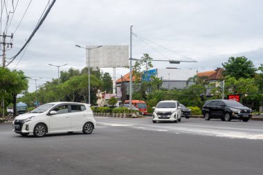 Bali, Endonezya - 22 Aralık 2024: Bali 'de kavşak. Beyaz araba arka planda reklam panosuyla caddeden aşağı doğru gidiyor..