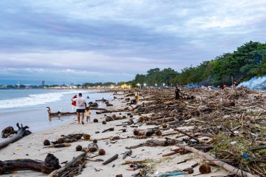 Bali, Endonezya - 22 Aralık 2024: Plaj çöplerle ve plajda yürüyen insanlarla dolu. Sahne artık el değmemiş ve güzel bir yer olmadığı için kasvetli ve hüzünlü.