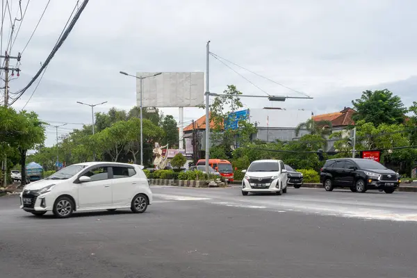 Bali, Endonezya - 22 Aralık 2024: Bali 'de kavşak. Beyaz araba arka planda reklam panosuyla caddeden aşağı doğru gidiyor..