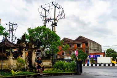 Bali, Endonezya - 10 Aralık 2024: Kadın bir tapınağın önünde yürüyor. Gökyüzü bulutlu ve cadde boş.