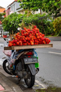 Bali, Endonezya - 10 Aralık 2024: Adam motosiklet üzerinde rambutan adı verilen meyveler satıyor. Meyve kırmızıdır ve onlardan çok var.