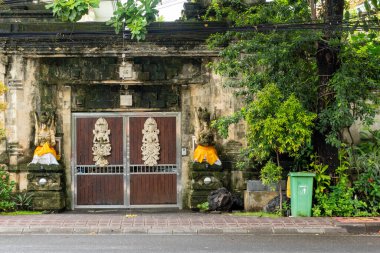 Bali, Endonezya - 10 Aralık 2024: Önünde yeşil bir çöp kutusu olan büyük bir bina. Binanın üzerinde bir sürü heykel var.