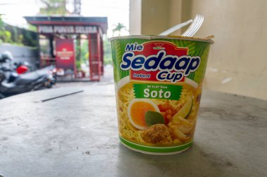 Bali, Endonezya - 10 Aralık 2024: Mie Sedap Soto 'nun küçük konteynırı bir masada bulunuyor. Konteynır yeşil ve beyaz ve üzerinde erişte ve et resmi var. Görüntünün rahat ve rahat bir havası var.