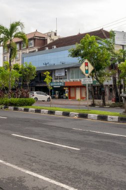 Bali, Endonezya - 10 Aralık 2024: Yoğun bir cadde ve bir kamyon geçiyor. Sokak ağaçlar ve binalarla dolu. Gökyüzü bulutlu ve güneş görünmüyor.