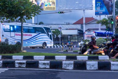 Bali, Endonezya - 10 Aralık 2024: Mavi beyaz otobüsü ve birkaç motosikleti olan işlek cadde. Otobüs sokağın solunda ve motosikletler de sağda.