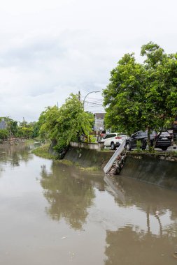 Bali, Endonezya - 28 Aralık 2024: Nehir iki ev arasında akıyor. Su bulanık ve evler de eski. Sahne kasvetli ve davetsiz.