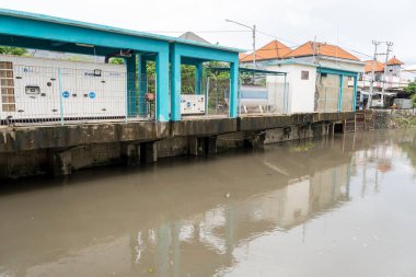 Bali, Endonezya - 28 Aralık 2024: Nehir iki ev arasında akıyor. Su bulanık ve evler de eski. Sahne kasvetli ve davetsiz.