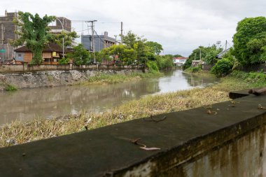 Bali, Endonezya - 28 Aralık 2024: Nehir iki ev arasında akıyor. Su bulanık ve evler de eski. Sahne kasvetli ve davetsiz.
