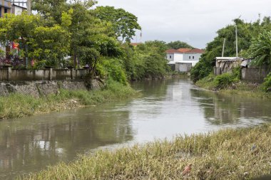 Bali, Endonezya - 28 Aralık 2024: Nehir iki ev arasında akıyor. Su bulanık ve evler de eski. Sahne kasvetli ve davetsiz.