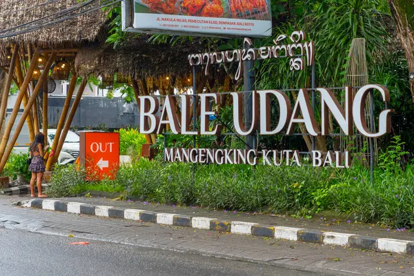 Bali, Endonezya - 10 Aralık 2024: Kadın Bale Udang yazan bir tabelanın önünde duruyor. İşaret yabancı bir dilde.