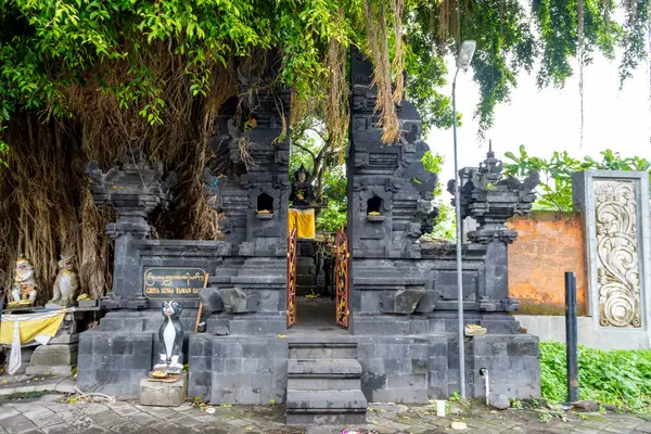 Bali, Endonezya - 10 Aralık 2024: Siyah beyaz renkli küçük bir türbe. Tapınak ağaçlarla çevrili ve taş bir yapısı var.