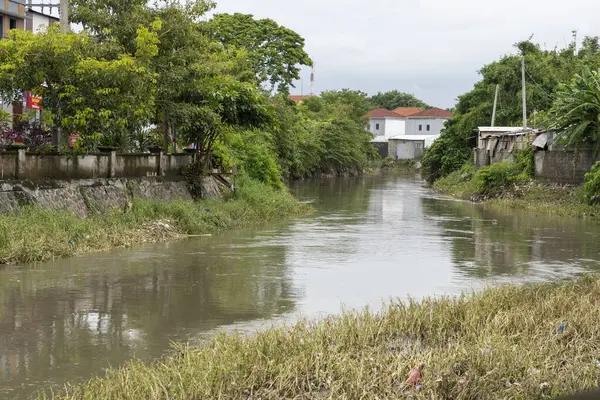 Bali, Endonezya - 28 Aralık 2024: Nehir iki ev arasında akıyor. Su bulanık ve evler de eski. Sahne kasvetli ve davetsiz.
