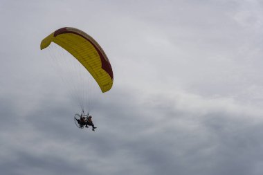 Bali, Endonezya - 13 Aralık 2024: Adam plajda sarı ve kırmızı bir paraşütle uçuyor. Gökyüzü bulutlu ve sahil insanlarla dolu.