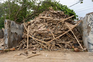 Ahşap ve çöp yığını duvara yığılmış. Yığın büyük ve dağınık, bazı odunlar kırılmış ve diğerleri hala iyi durumda. Sahne düzensizlik hissi veriyor.