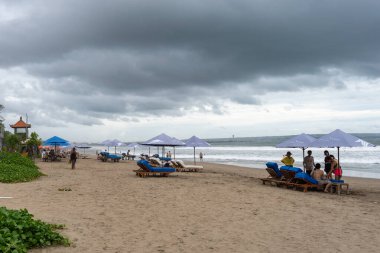 Bali, Endonezya - 11 Aralık 2024: Şemsiyeler altında birçok insanla plaj. Sahil kalabalık ve hareketli. İnsanlar güneşin ve okyanusun tadını çıkarıyorlar.