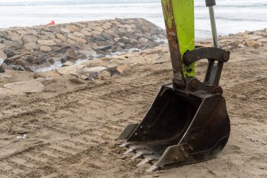 Yeşil saplı Escavator kovası kumu kazıyor. Makine okyanusa yakın bir sahilde.