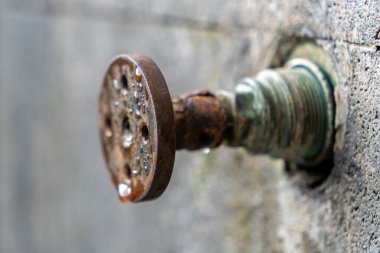 İçinden su damlayan paslı musluk. Su damlacıkları küçük ve dağınıktır, hafif yağmur izlenimi verir. Musluk eski ve yıpranmış, paslı bir görünüme sahip.