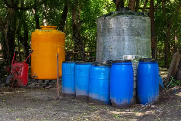 Bir grup mavi fıçı ve sarı fıçı bir tarlada oturuyorlar. Fıçılar üst üste istiflenmiş, ortada da sarı varil var. Sahnenin bir köylüsü var.