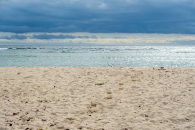Arka planda bulutlu bir gökyüzü olan plaj. Gökyüzü bulutlu ve su sakin.