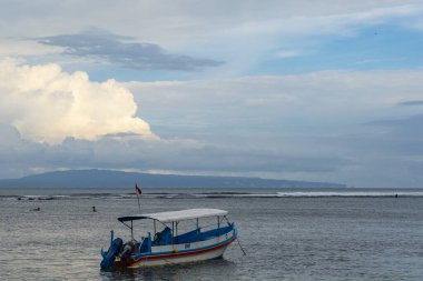 Bali, Endonezya - 17 Aralık 2024: Küçük mavi tekne suda duruyor. Gökyüzü bulutlu ve su sakin.