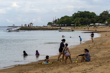 Bali, Endonezya - 17 Aralık 2024: Kumda oturup oynayan insanların olduğu plaj sahnesi. Sahne rahat ve sakin.